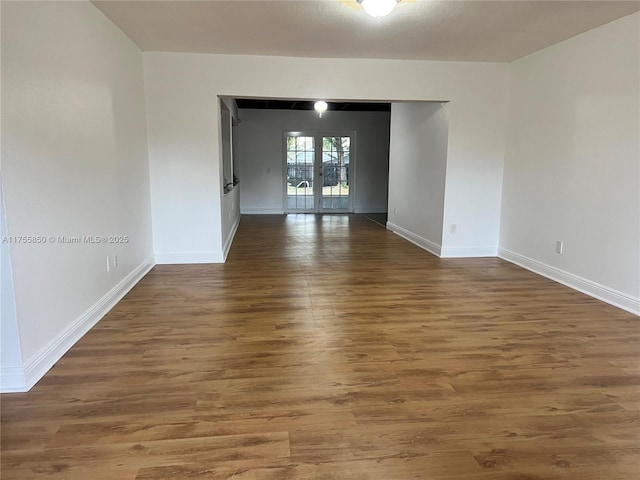 empty room with baseboards, wood finished floors, and french doors