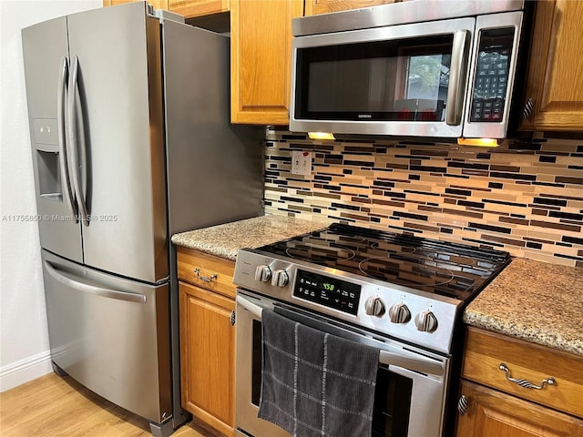 kitchen featuring stainless steel appliances, light wood-style floors, decorative backsplash, and light stone countertops