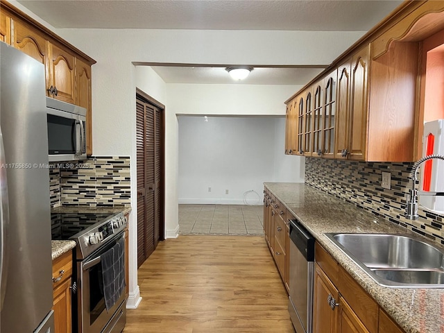 kitchen with appliances with stainless steel finishes, light wood-style floors, brown cabinetry, and a sink