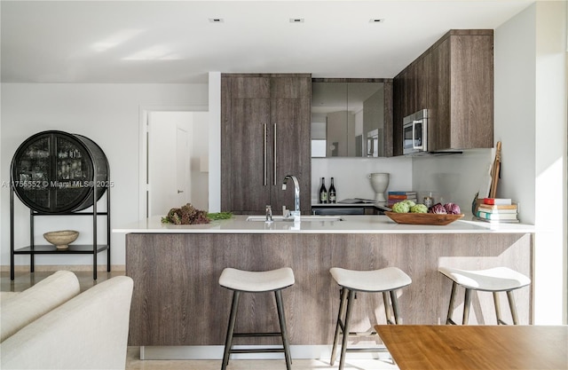 kitchen with a breakfast bar, a sink, light countertops, stainless steel microwave, and modern cabinets