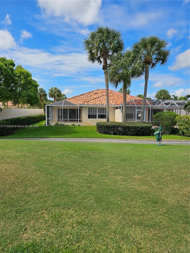 view of front facade featuring a front yard, glass enclosure, a tiled roof, and stucco siding