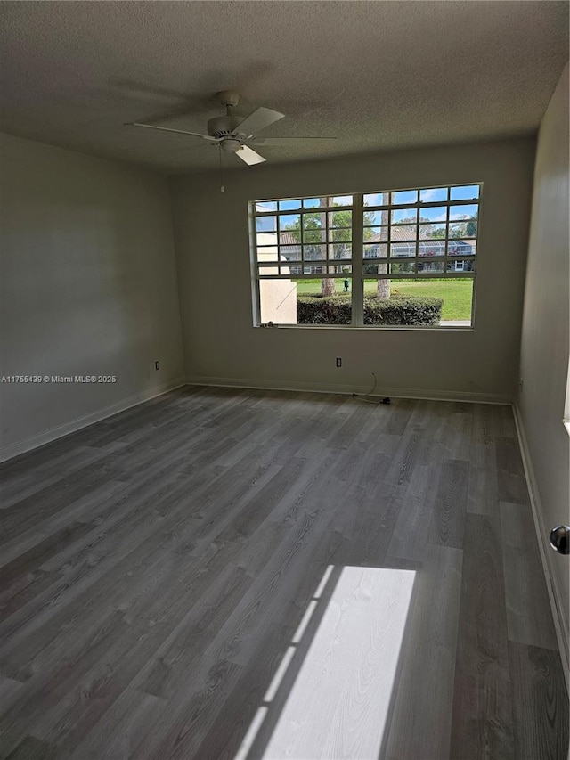 empty room with a textured ceiling, wood finished floors, a wealth of natural light, and baseboards