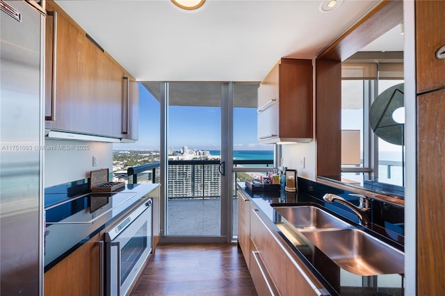 kitchen with dark wood-type flooring, brown cabinetry, a sink, and built in appliances