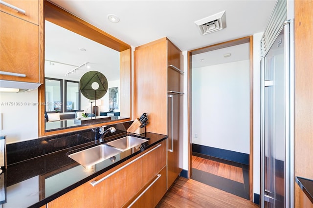 kitchen featuring brown cabinets, rail lighting, a sink, wood finished floors, and baseboards