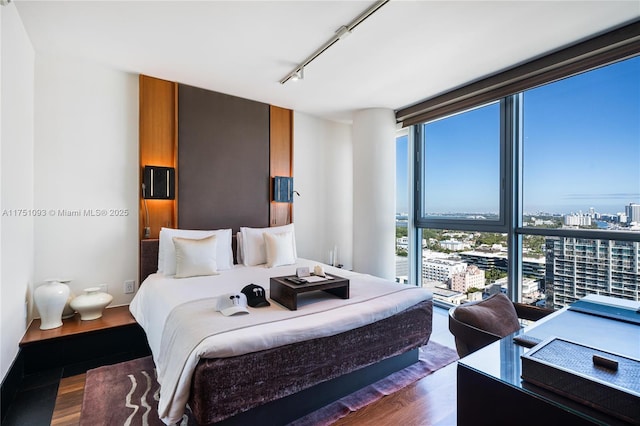 bedroom with dark wood-style floors, floor to ceiling windows, a city view, and track lighting