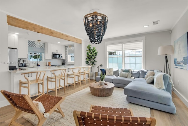 living area featuring ornamental molding, light wood-type flooring, visible vents, and baseboards