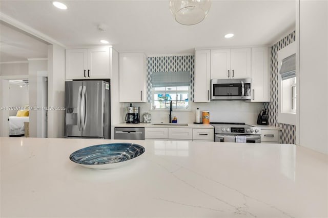 kitchen with light stone countertops, stainless steel appliances, white cabinetry, a sink, and recessed lighting