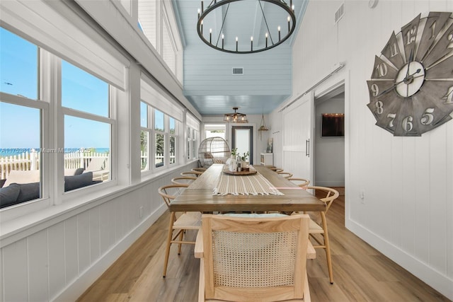 dining space with a chandelier, visible vents, light wood-style floors, and a high ceiling