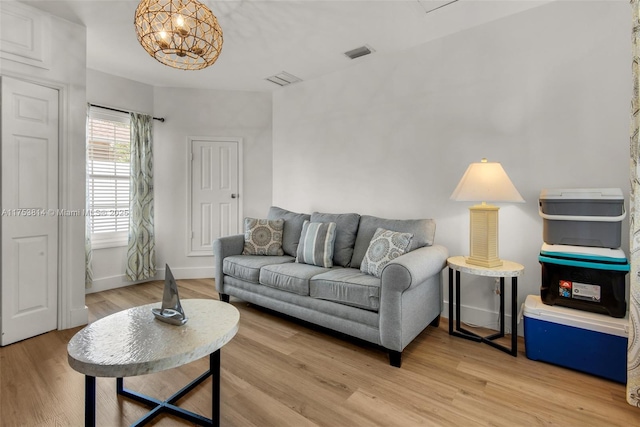 living room featuring a notable chandelier, light wood-type flooring, visible vents, and baseboards