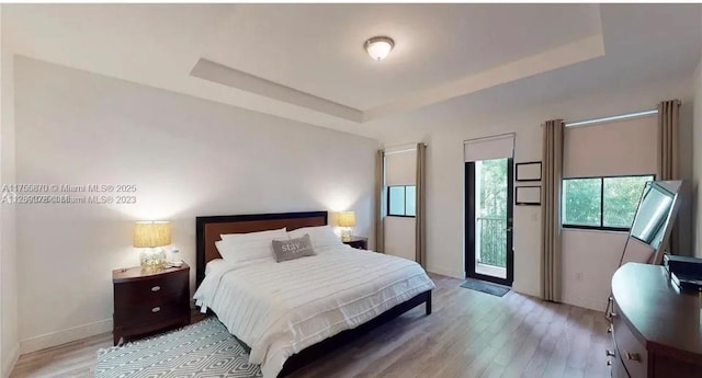 bedroom with a raised ceiling, light wood-style flooring, and baseboards