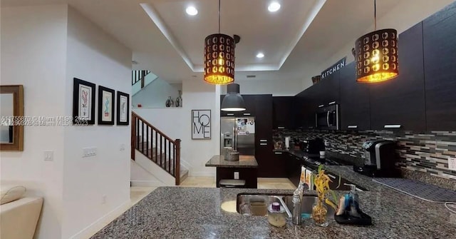 kitchen featuring a raised ceiling, backsplash, appliances with stainless steel finishes, a kitchen island, and dark cabinets