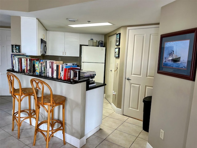 2351 Douglas Rd Unit 1109, Miami, FL 33145 - kitchen featuring freestanding refrigerator, a peninsula, light tile patterned floors, white cabinetry, and black microwave