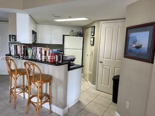 kitchen featuring white cabinets, dark countertops, stainless steel microwave, a peninsula, and a kitchen bar