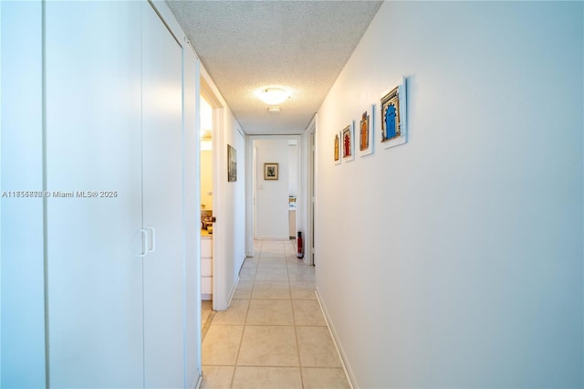 corridor featuring a textured ceiling, baseboards, and light tile patterned floors