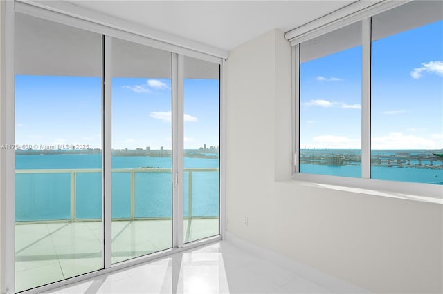 empty room featuring baseboards, a water view, tile patterned flooring, and floor to ceiling windows