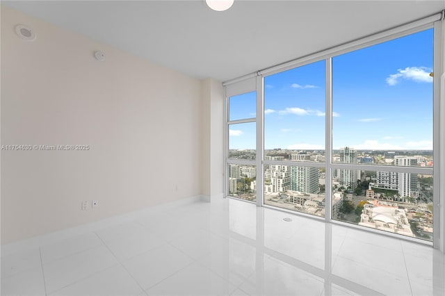 tiled empty room featuring floor to ceiling windows, a city view, and baseboards