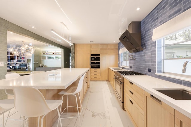 kitchen with light brown cabinets, wall chimney range hood, stainless steel stove, marble finish floor, and a sink