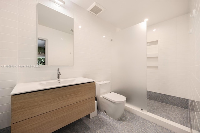 full bathroom with visible vents, toilet, a tile shower, tile walls, and vanity