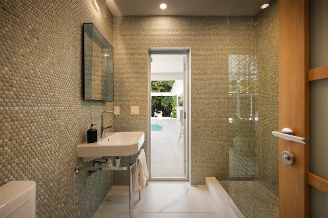 bathroom featuring a walk in shower, toilet, tile walls, and a sink