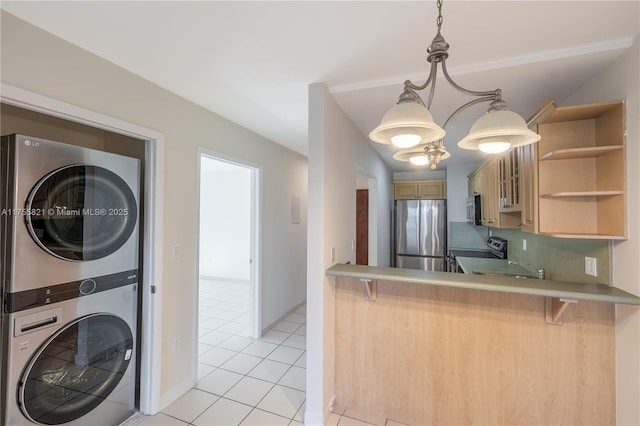 kitchen featuring light tile patterned floors, a breakfast bar, stacked washer / dryer, light countertops, and appliances with stainless steel finishes