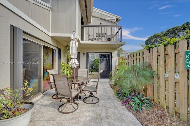 view of patio with outdoor dining area, fence, and a balcony