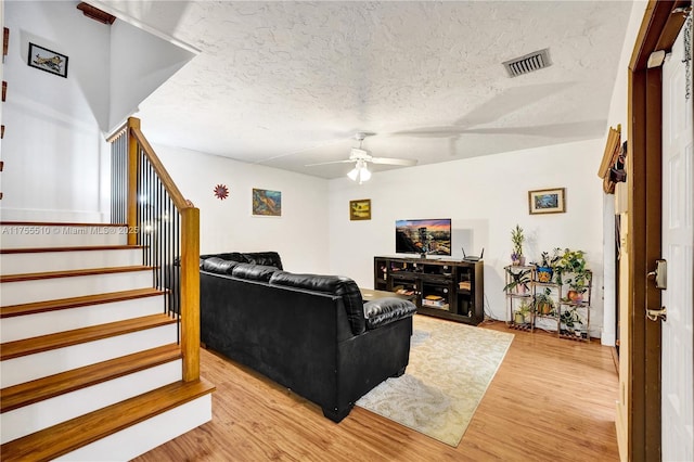 living area with a textured ceiling, stairway, visible vents, and light wood-style floors