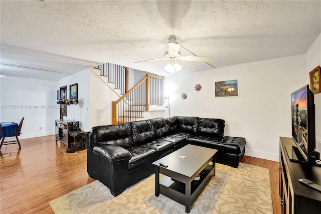 living area with a textured ceiling, stairway, baseboards, and light wood-style floors