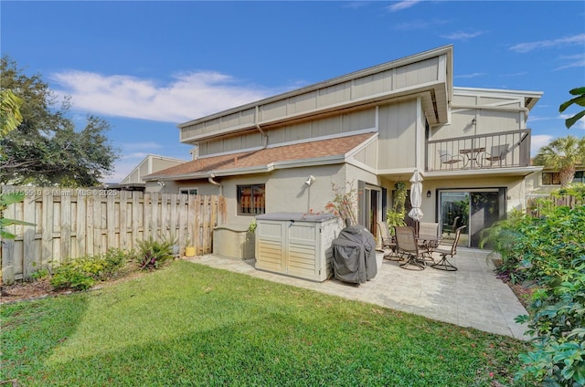 rear view of property with a balcony, fence, a lawn, stucco siding, and a patio area