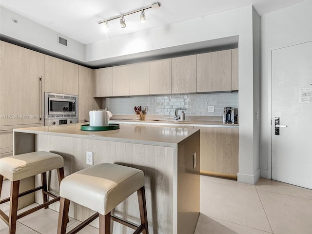 kitchen with a breakfast bar, a sink, visible vents, backsplash, and stainless steel microwave