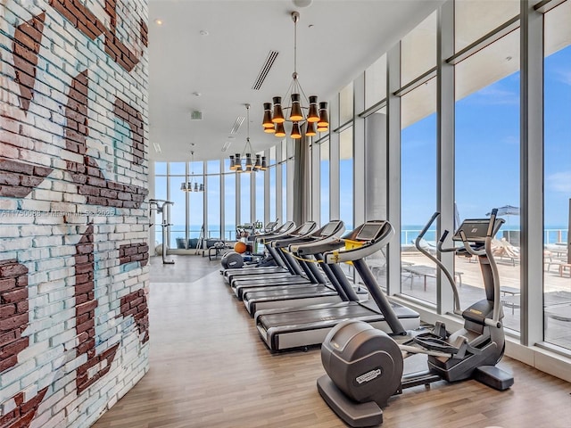 workout area with a notable chandelier, brick wall, visible vents, floor to ceiling windows, and light wood finished floors