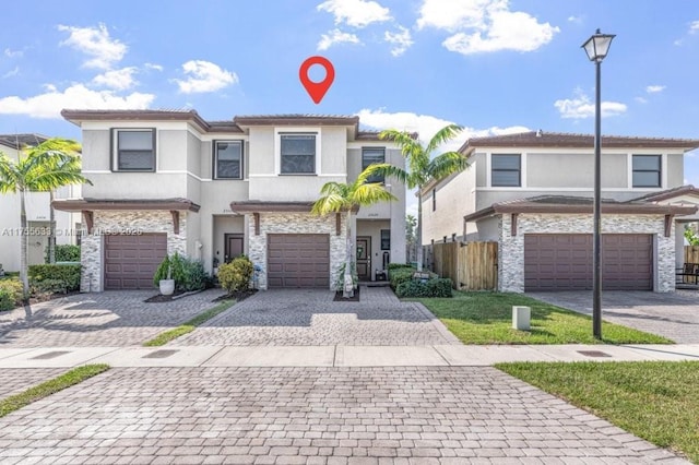 townhome / multi-family property with an attached garage, stone siding, decorative driveway, and stucco siding