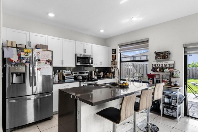 kitchen featuring light tile patterned flooring, stainless steel appliances, a sink, white cabinetry, and dark countertops