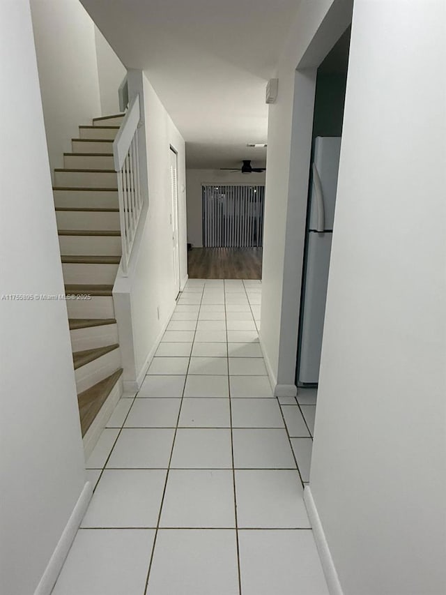 hallway featuring stairway, light tile patterned flooring, and baseboards