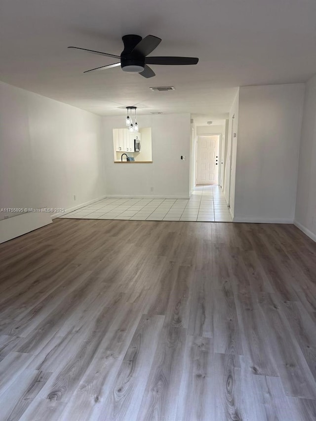 empty room with ceiling fan, visible vents, baseboards, and wood finished floors