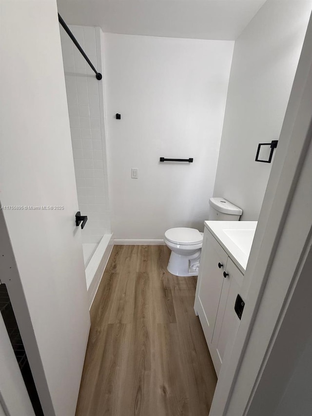 bathroom featuring toilet, wood finished floors, a tile shower, baseboards, and vanity