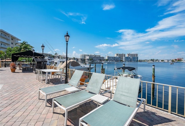 view of dock with a water view, a patio area, outdoor dining area, and a city view