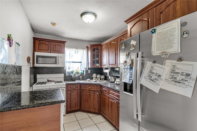 kitchen with light tile patterned floors, a textured ceiling, white appliances, a sink, and glass insert cabinets