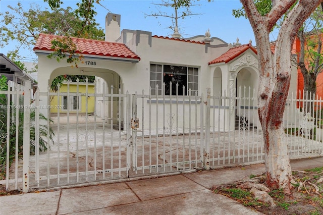 view of front of property featuring a fenced front yard, a tiled roof, a gate, stucco siding, and a chimney