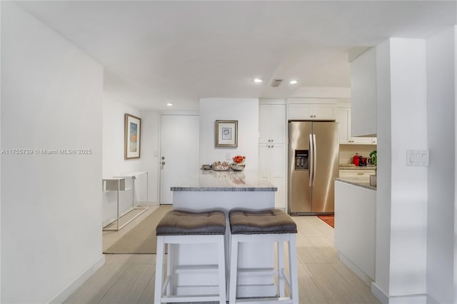 kitchen with baseboards, white cabinets, stainless steel fridge with ice dispenser, light stone counters, and recessed lighting