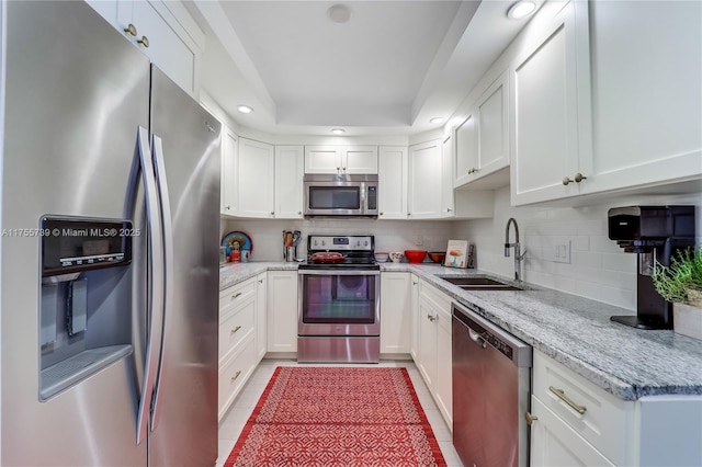 kitchen featuring decorative backsplash, light stone countertops, stainless steel appliances, white cabinetry, and a sink