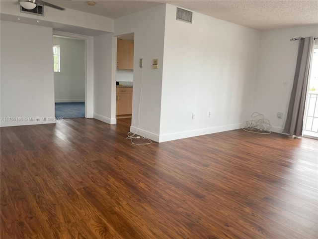 empty room featuring baseboards, visible vents, dark wood finished floors, and a textured ceiling