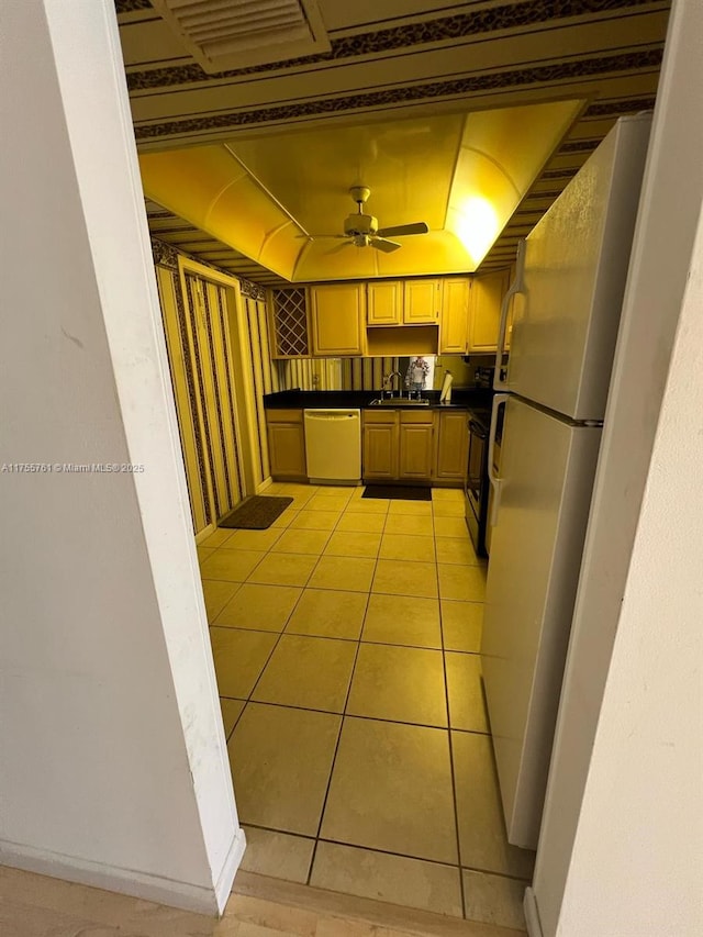 kitchen featuring white appliances, light tile patterned floors, dark countertops, ceiling fan, and a sink