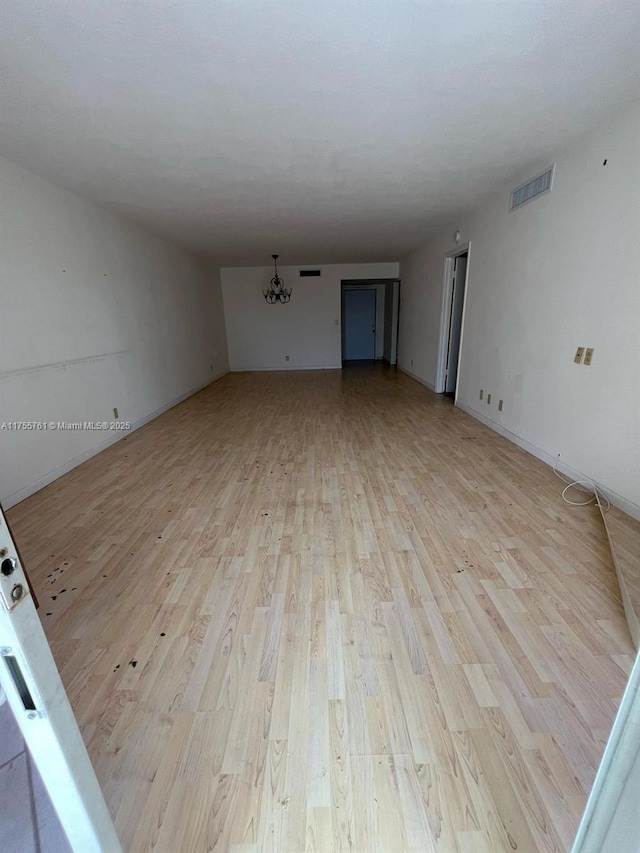 empty room featuring visible vents, an inviting chandelier, and light wood finished floors