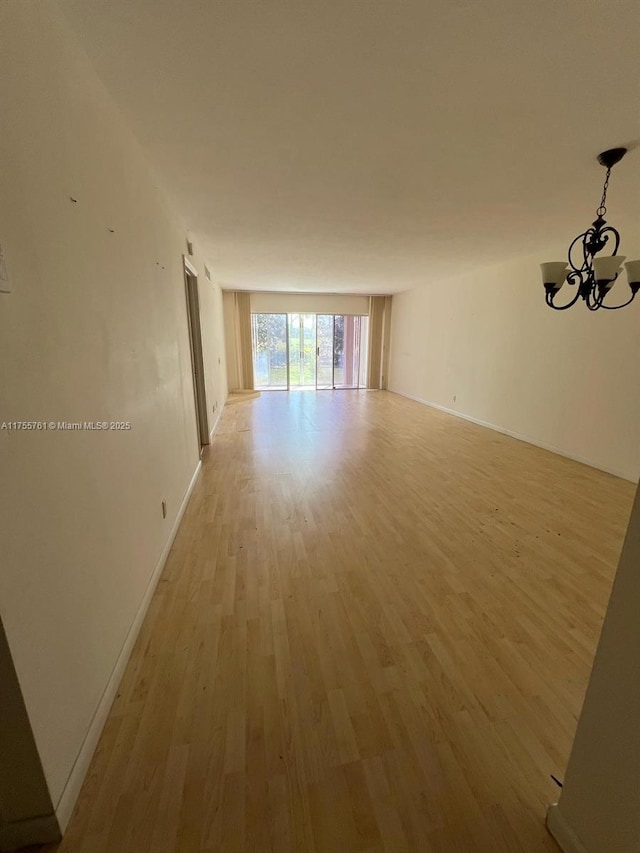 unfurnished room featuring baseboards, a notable chandelier, and light wood finished floors