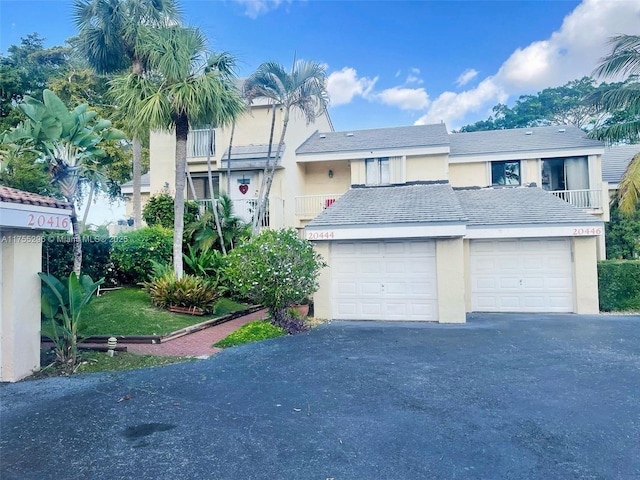 townhome / multi-family property featuring a garage, a balcony, aphalt driveway, and stucco siding