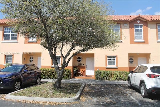 townhome / multi-family property with stucco siding, a tile roof, and uncovered parking