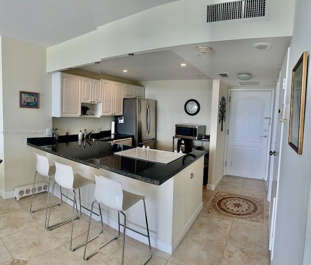 kitchen featuring dark countertops, visible vents, appliances with stainless steel finishes, a peninsula, and a kitchen bar