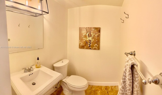 half bath featuring a sink, toilet, and baseboards