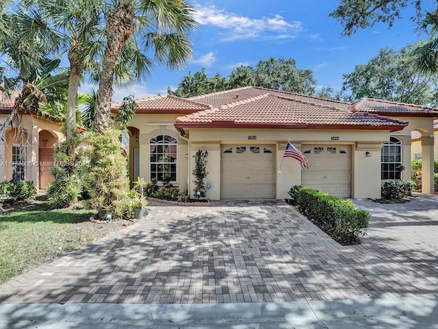 mediterranean / spanish-style home with decorative driveway, a tile roof, an attached garage, and stucco siding