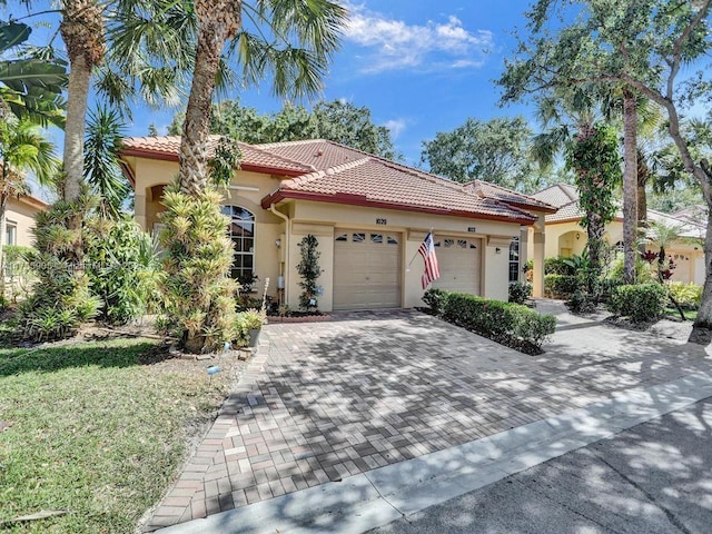 mediterranean / spanish-style house featuring a garage, decorative driveway, a tiled roof, and stucco siding